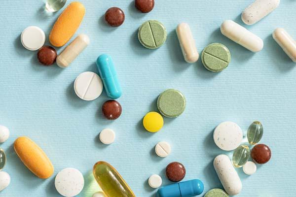 Overhead view of assorted vitamins and nutritional supplements in various shapes and colors, scattered randomly on a light blue surface.