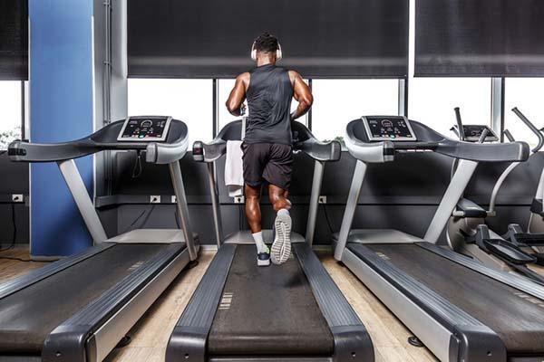 View from behind of a man running on a treadmill in a gym while wearing headphones.