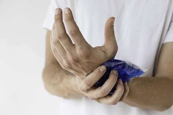 Cropped image showing arms and hands of a man holding an ice pack on his wrist.