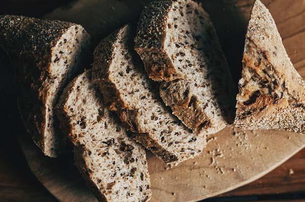 Close-up of a sliced loaf of multi-grain bread on a wood surface.
