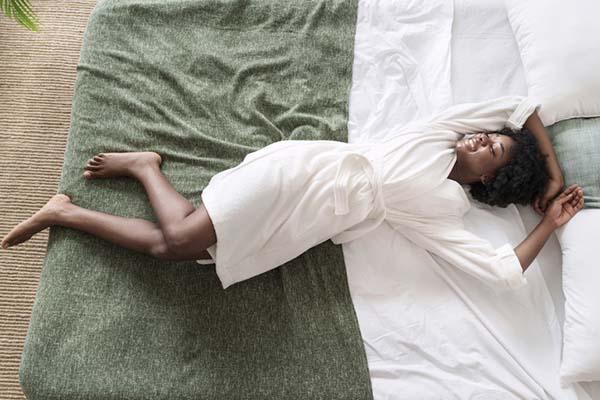 Overhead view of a woman in a white robe smiling and relaxing on her bed.