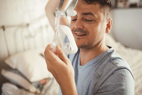 A man in the process of attaching a CPAP mask for sleep apnea to his face and head.