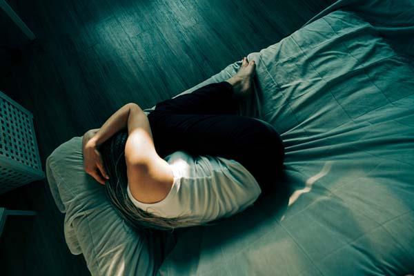 Overhead view of a long-haired woman curled into a fetal position on a couch, with her hands on top of her head.