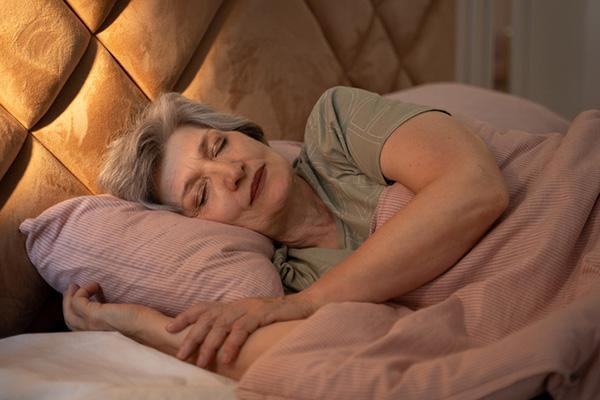 A mature woman sleeps on her side, with the glow of a soft light coming from the left side.