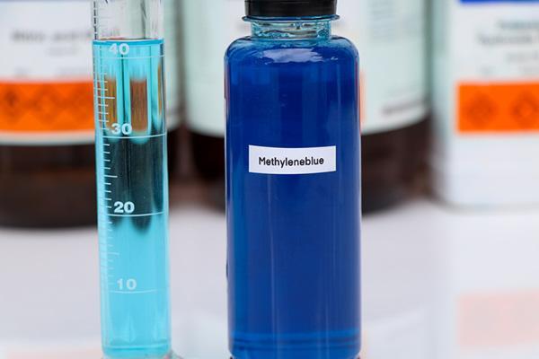 A glass bottle containing blue liquid, with a label reading methyleneblue; standing next to it is a test tube marked in milliliters.