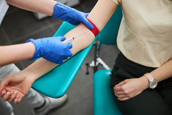 Cropped photo of the gloved hands of a nurse inserting a needle into the arm of a patient.