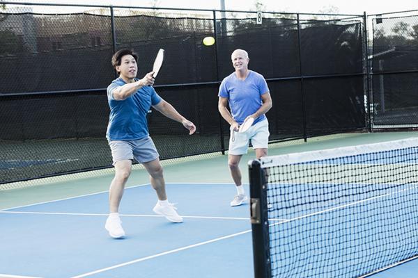 Two men, one mature and one around 30, play pickleball as a doubles team.
