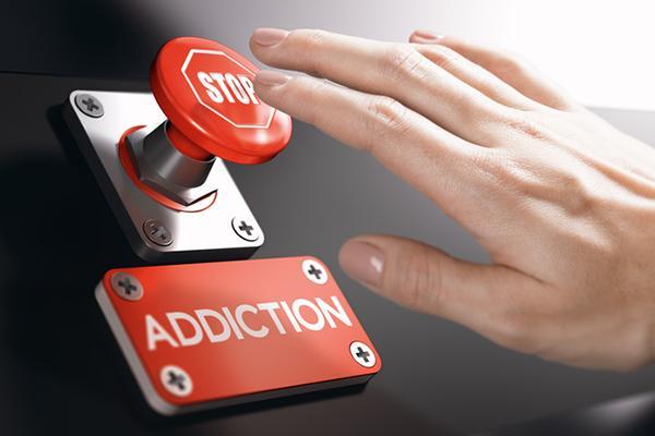 A woman's hand reaches toward a red button labeled stop, with a red sign under the button that reads addiction.