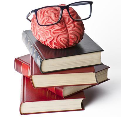 A model of a human brain with eyeglasses on it rests on top of a stack of hard cover books.