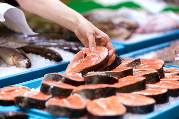 A hand reaches to select a salmon steak from a tray in a fish market.