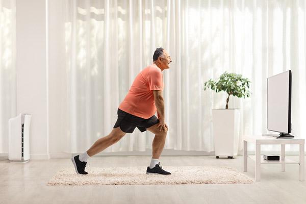 A mature man doing stretches in front of a TV in his home.
