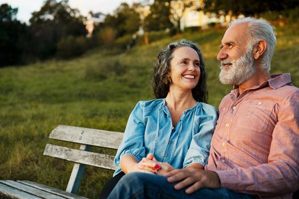 A mature couple sitting on a bench in a park, smiling and enjoying the day.