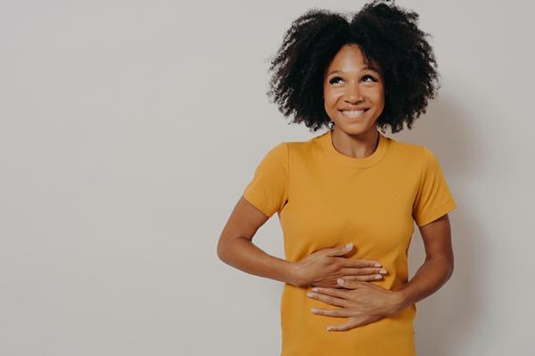 A young woman smiles and looks to one side, looking embarrassed, as she holds both hands to her stomach.