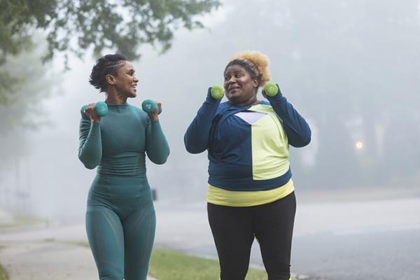 Two women exercising with hand weights outdoors in the morning, with fog obscuring a house in the background.