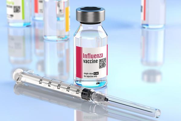 A vial containing influenza vaccine on a counter with an unused syringe laid in front of it.