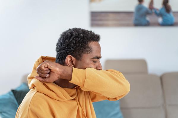 A man covers his mouth with his arm while coughing.