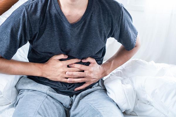 Cropped (head not visible) man holding both hands to his stomach, experiencing stomach pain.