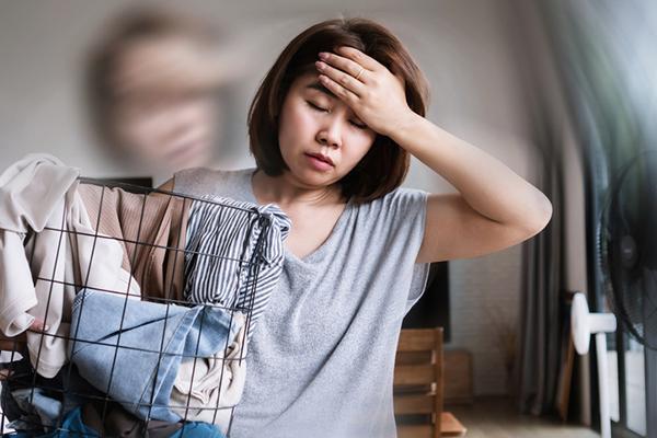 A woman feeling the effects of dizziness holds a hand to her forehead while carrying a laundry basked with her other arm.
