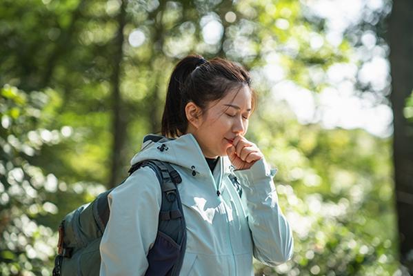 A young woman walking in the woods holds a hand in front of her mouth.