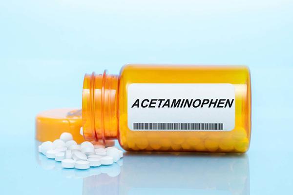 An orange medication bottle labeled acetaminophen, on its side with the cap off and pills spilled out.