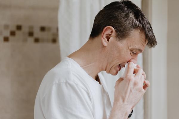 Side view of a man holding a tissue to his nose.