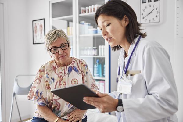 A doctor holding a tablet shares test results with a patient in an examination room.