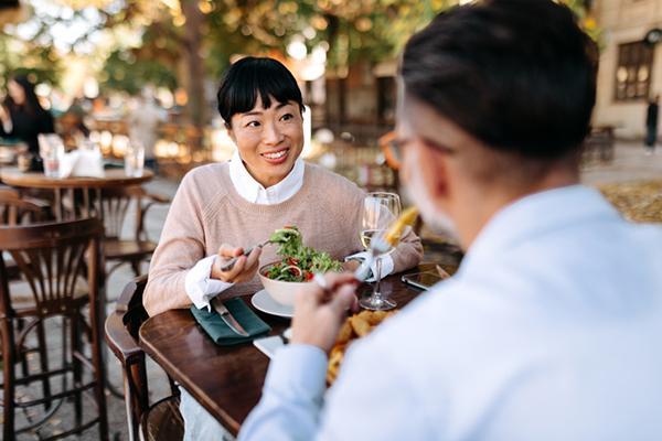 A couple enjoying a meal at an outdoor cafe. Sunlight can be seen in the background but the seating area is shaded.