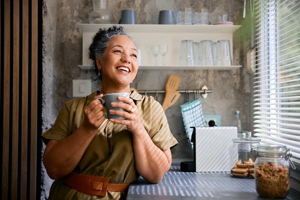 A woman smiles as she enjoys a cup of coffee in her kitchen.