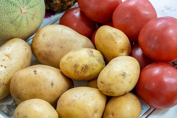 A small pile of freshly picked potatoes with some tomatoes behind them.