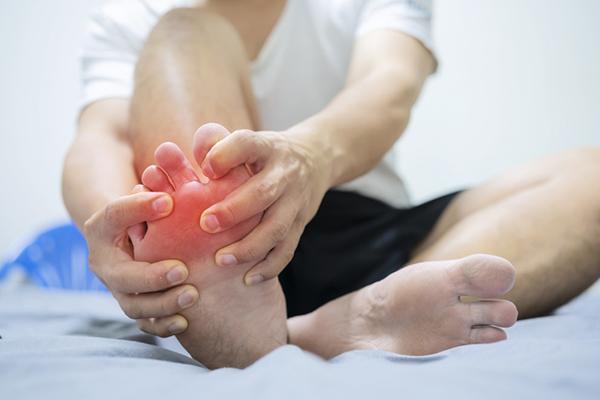 Close-up of the lower body of a man holding his foot with both hands; the foot is red with pain.