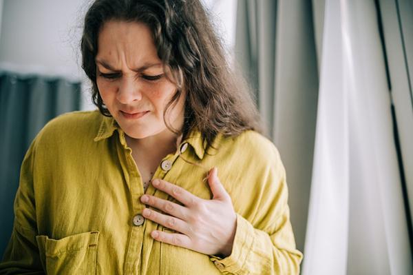 A woman suffering from chest pain, grimacing and holding her hand over her heart.