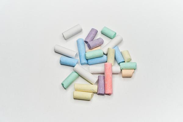 A pile of pieces of chalk in assorted colors and different lengths rests on a white background.