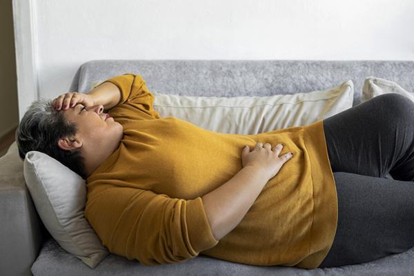 A woman experiencing stomach cramps lies on a couch with one hand over her abdomen.