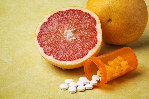 Close-up of half a grapefruit next to a whole one, with an orange medication bottle on its side spilling out pills.