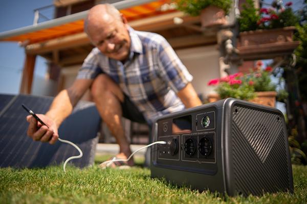 A senior man uses a portable generator to charge his phone in his backyard.
