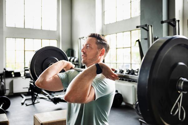 A man uses a barbell while performing a squat exercise in a gym.