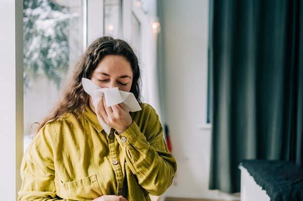 A woman blows her nose into a tissue.