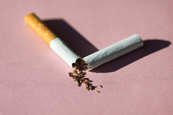 A broken cigarette rests on a pink surface.