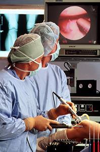 A surgeon performs arthroscopic surgery on a person's knee, looking at a monitor showing an image from a camera inserted into the knee..