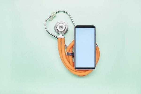 Overhead view of a smartphone on top of a coiled stethoscope, both resting on a pale green surface.