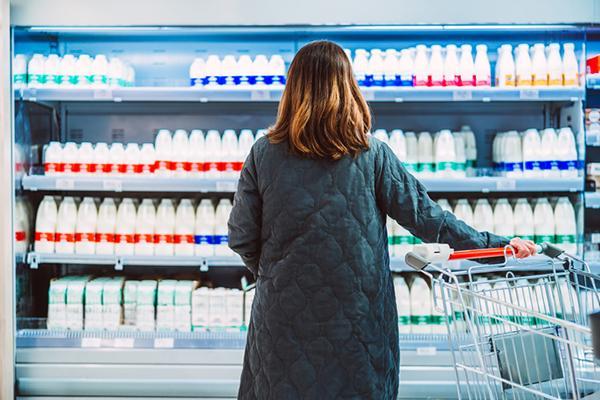 View from behind of a woman standing in front of the dairy case in a supermarket with rows of bottled milk.