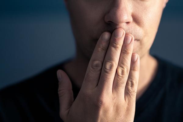 A man covers his mouth with his hand, held with the fingers vertical.