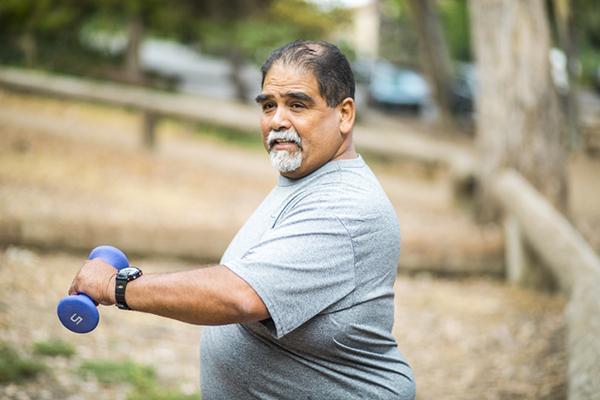 A mature man works out with hand weights in an outdoor setting.