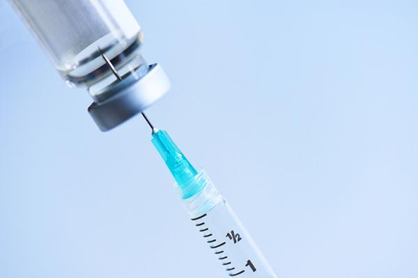 Close-up of a syringe inserted into a vial holding liquid medication, against a light blue background.
