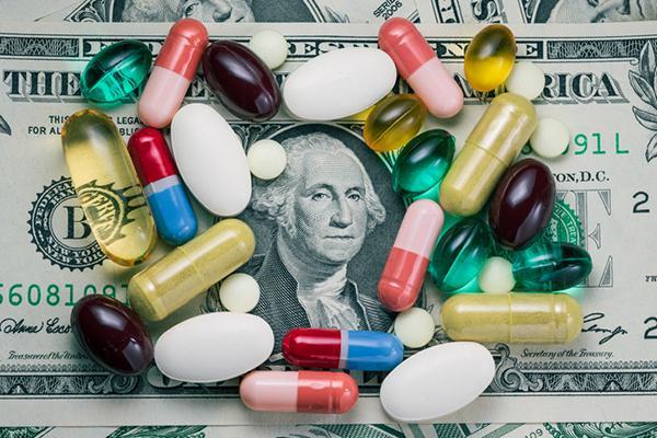 Pills in assorted sizes, shapes, and colors, arranged on a dollar bill around the center portrait of George Washington.
