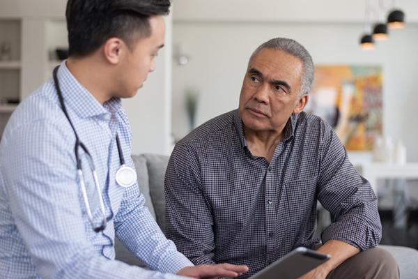 A male nurse meets with a mature male patient in the man's home