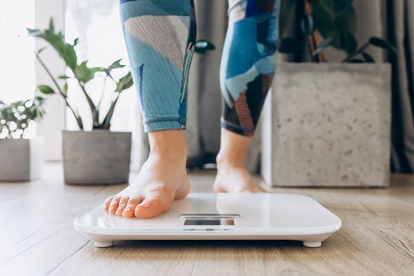Close-up of the lower legs and bare feet of a woman stepping onto a scale.