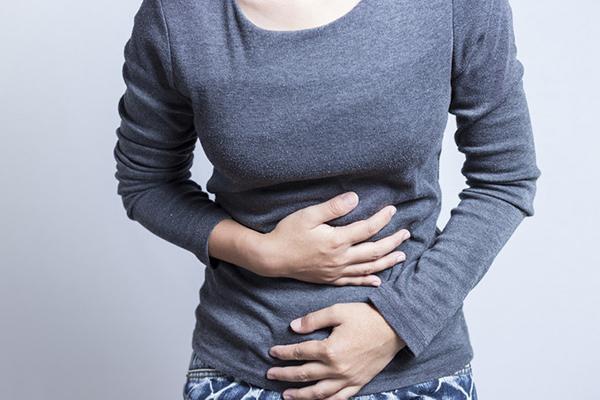 Cropped image shows the torso of a woman clutching her stomach with both arms.