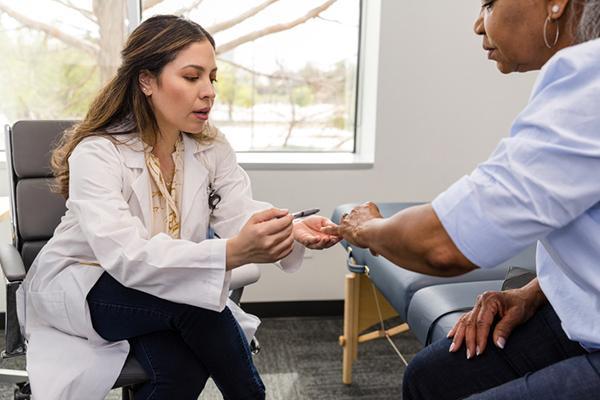A doctor examines her patient's hand while pointing with a pen and speaking to her.