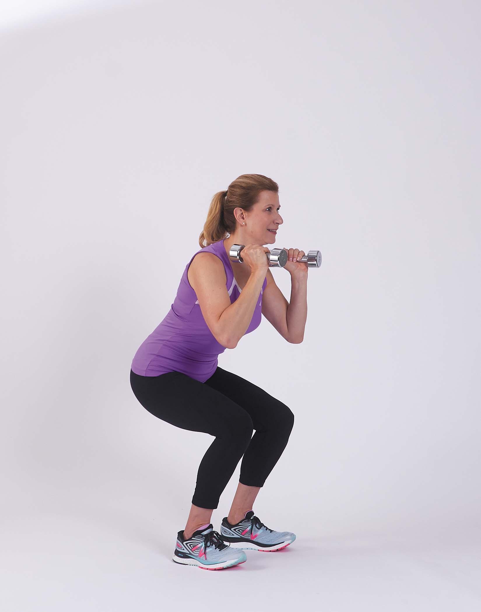 A woman demonstrates the movement for the squat with weights exercise as described in the article.